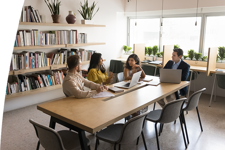 Multiethnic small team of business colleagues talking in academic co-working space, discussing teamwork at large table. Group of adult students meeting in library, brainstorming on training project